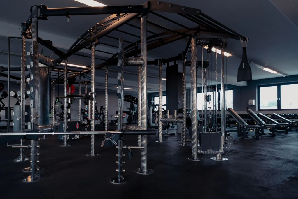 Ein moderner Fitnessbereich mit vielseitigen Kraft- und Trainingsgeräten, inklusive einer Seilzugstation, Functional Fitnessbereich und einem Boxsack.