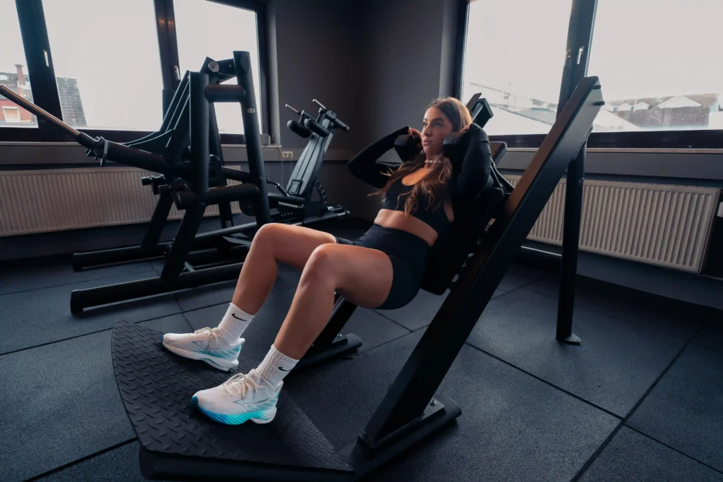 Eine Frau trainiert auf einer schrägen Beinpressenmaschine in einem modernen Fitnessstudio, fokussiert auf ihre Beinmuskulatur.