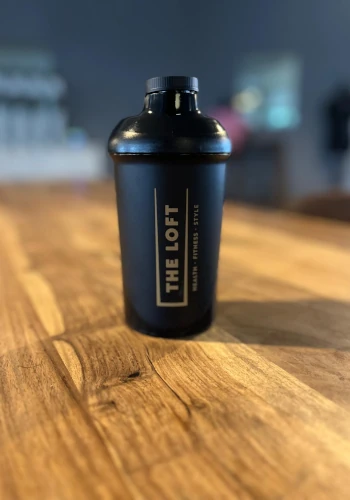 The Loft Shaker – Schwarzer Shaker mit "The Loft"-Branding, stehend auf einem Holztisch.