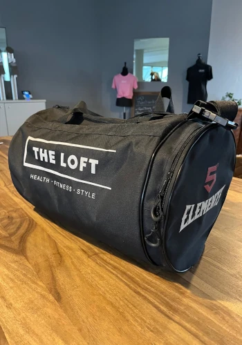 The Loft Sporttasche – Schwarze Sporttasche mit "The Loft"- und "5 Elements"-Branding, auf einem Holztisch platziert.