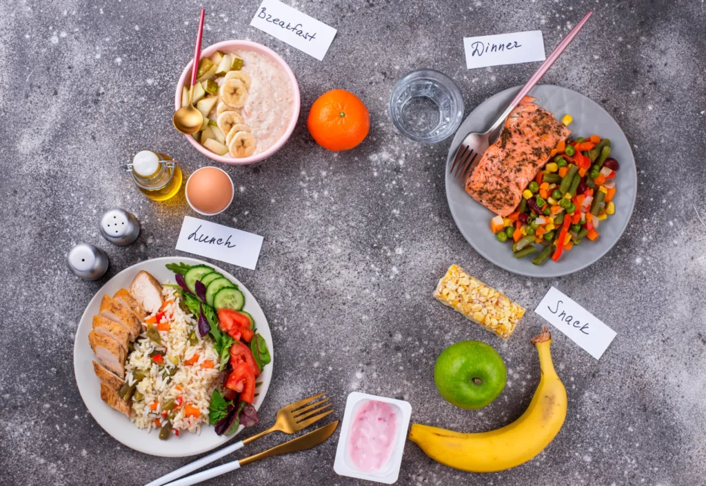 Ausgewogene Mahlzeiten für den Tag: Frühstück mit Obst und Porridge, Mittagessen mit Hähnchen und Reis, Abendessen mit Lachs und Gemüse, gesunde Snacks wie Obst und Joghurt.