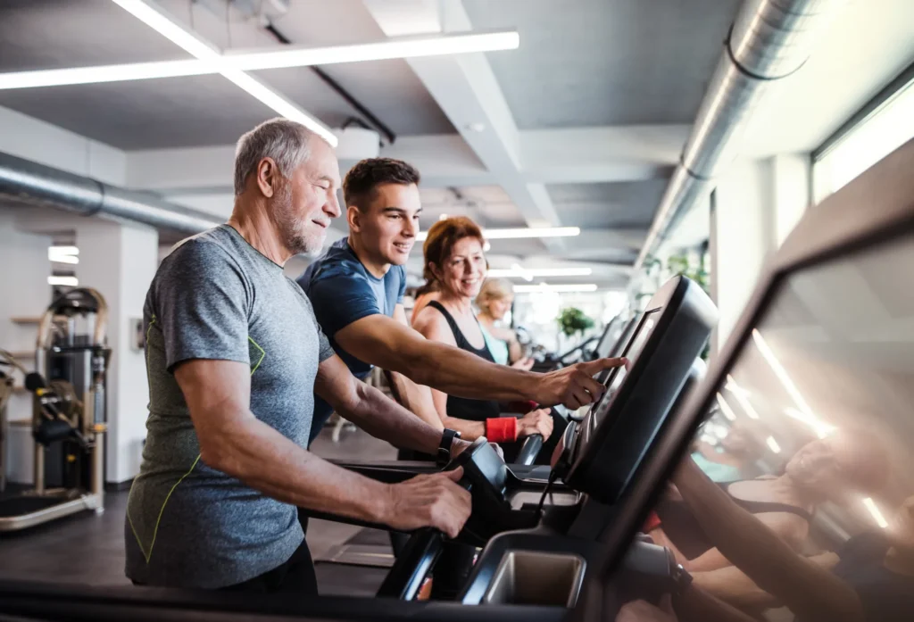 Älterer Mann trainiert mit Unterstützung eines Trainers auf dem Laufband im Fitnessstudio – Symbol für gesundes Altern und individuelles Training.