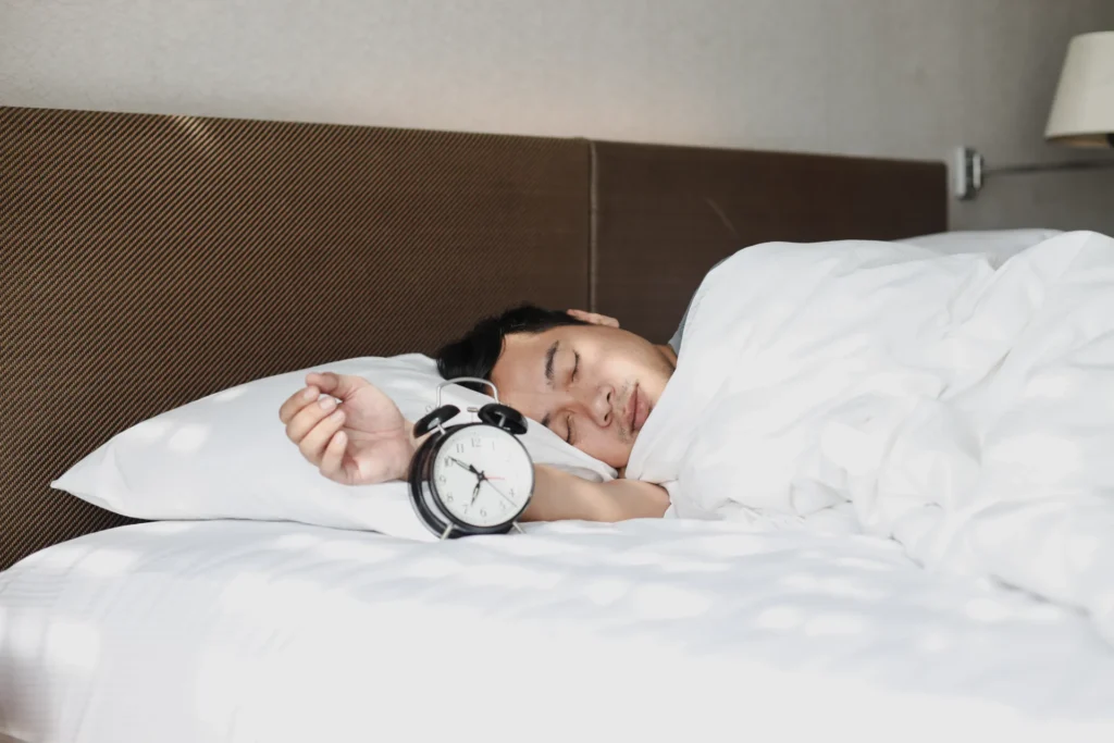 Mann schläft entspannt mit Wecker im Bett – Symbol für die Bedeutung von Schlaf bei Fettabbau und Muskelregeneration