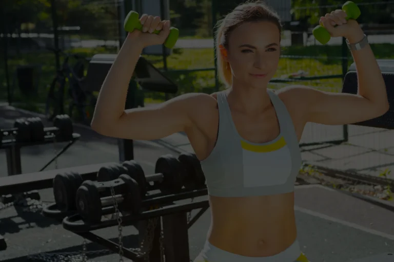Sportliche Frau beim Krafttraining mit Kurzhanteln im Outdoor-Gym bei Sonnenschein – Symbolbild für sommerliches Fitnesstraining