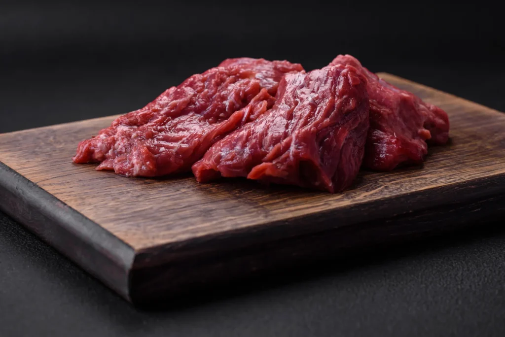 Rohes Rindfleisch auf einem dunklen Holzbrett – eiweißreiche Zutat für Muskelaufbau-Mahlzeiten