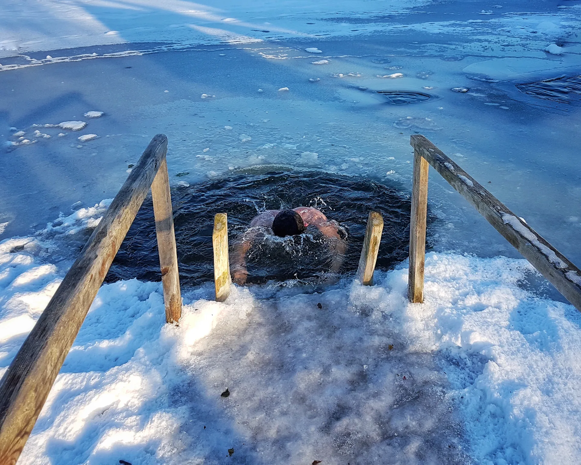 Sportler steigt nach der Sauna in ein Eisloch zur Abkühlung und Stärkung des Kreislaufs.