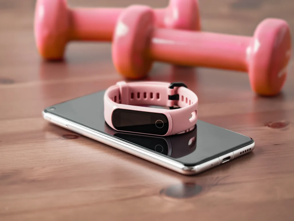 Fitnessarmband liegt auf Smartphone mit Hanteln im Hintergrund