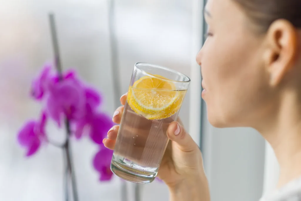 Frau trinkt morgens ein Glas Wasser mit Zitrone – Symbol für Hydration, Stoffwechselaktivierung und gesunden Start in den Tag