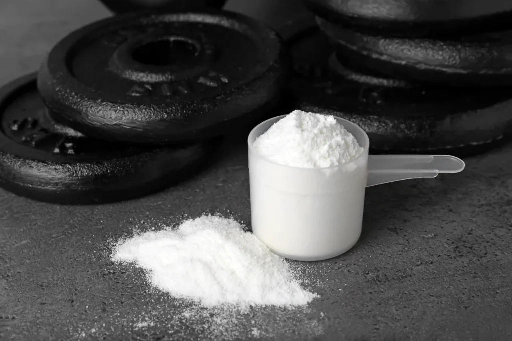 Kreatin Monohydrat Pulver in Messlöffel im Fitnessstudio neben Hantelscheiben