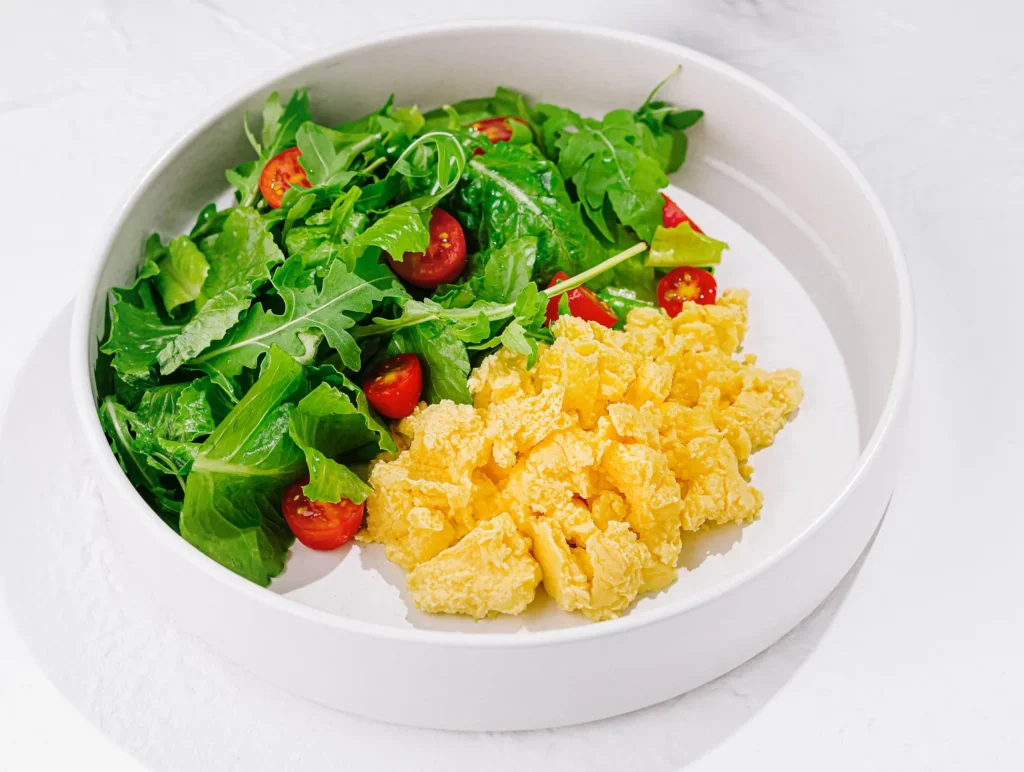 Rührei mit grünem Salat und Cherrytomaten in weißer Schale
