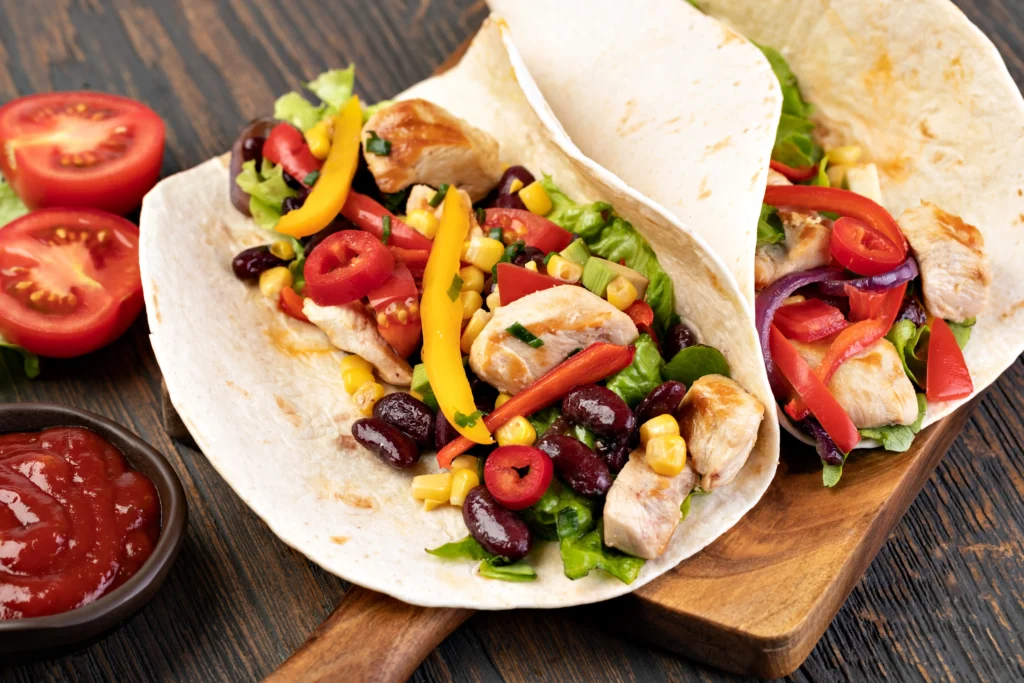 Gefüllte Chicken-Wraps mit Hähnchen, Paprika, Bohnen, Mais und frischem Salat auf Holzbrett – proteinreiche und gesunde Mahlzeit