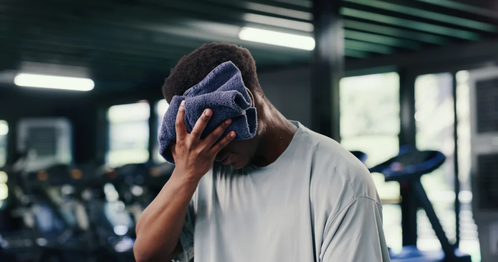 Erschöpfter Sportler wischt sich nach dem Training im Fitnessstudio mit einem Handtuch den Schweiß ab.